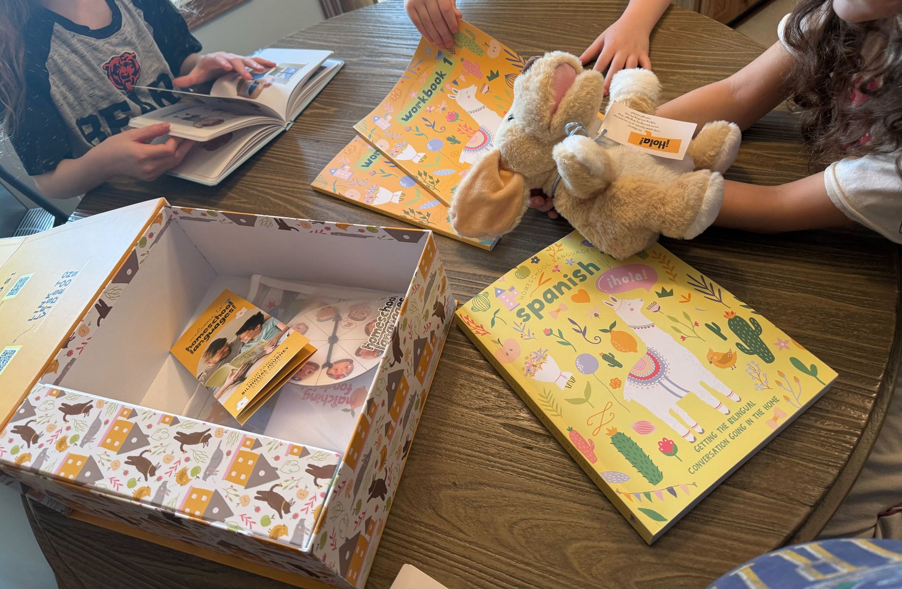 Kids sit around a table playing with Alberto the puppet and Spanish books